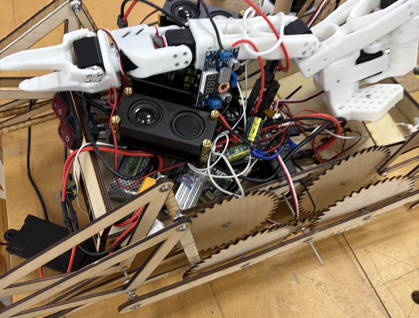 Single Jansen leg on a plywood test rig: white 3D-printed linkage links with exposed red and black wiring and a black controller box clamped to the rig